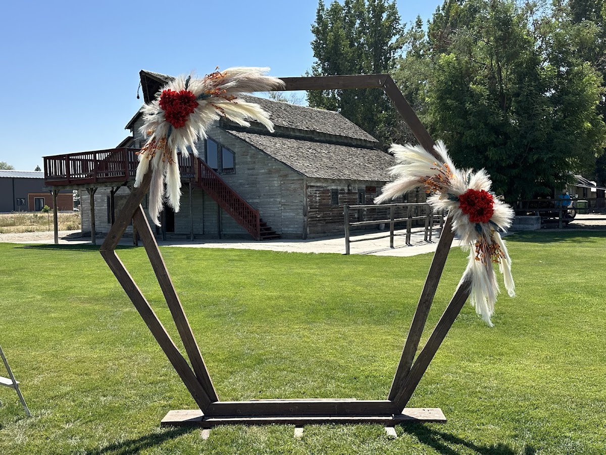 A wooden wedding ceremony arch dressed with pampas grass and red blooms at a Pendleton venue