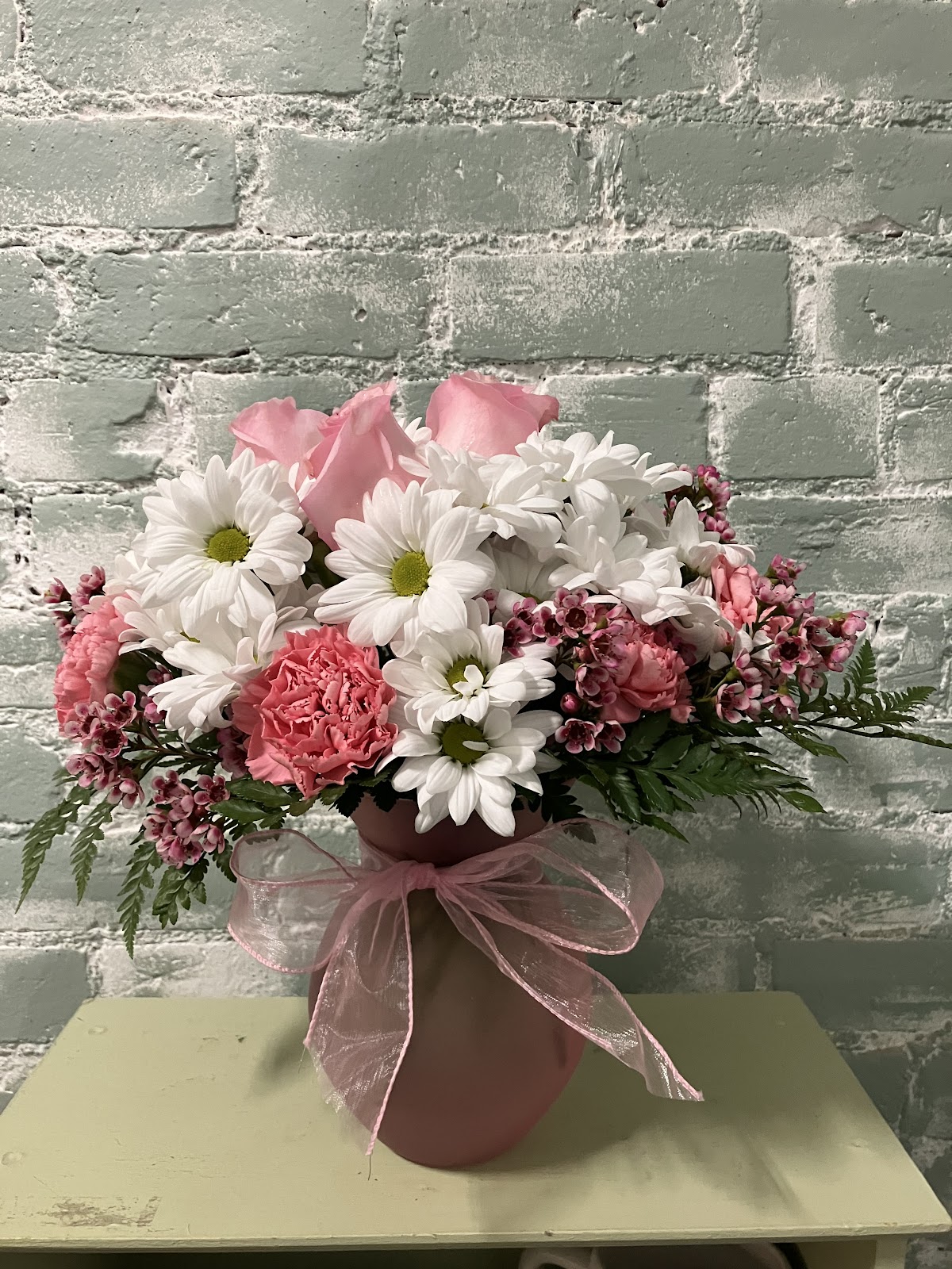 A soft pink and white arrangement against the shop's sage-green brick wall